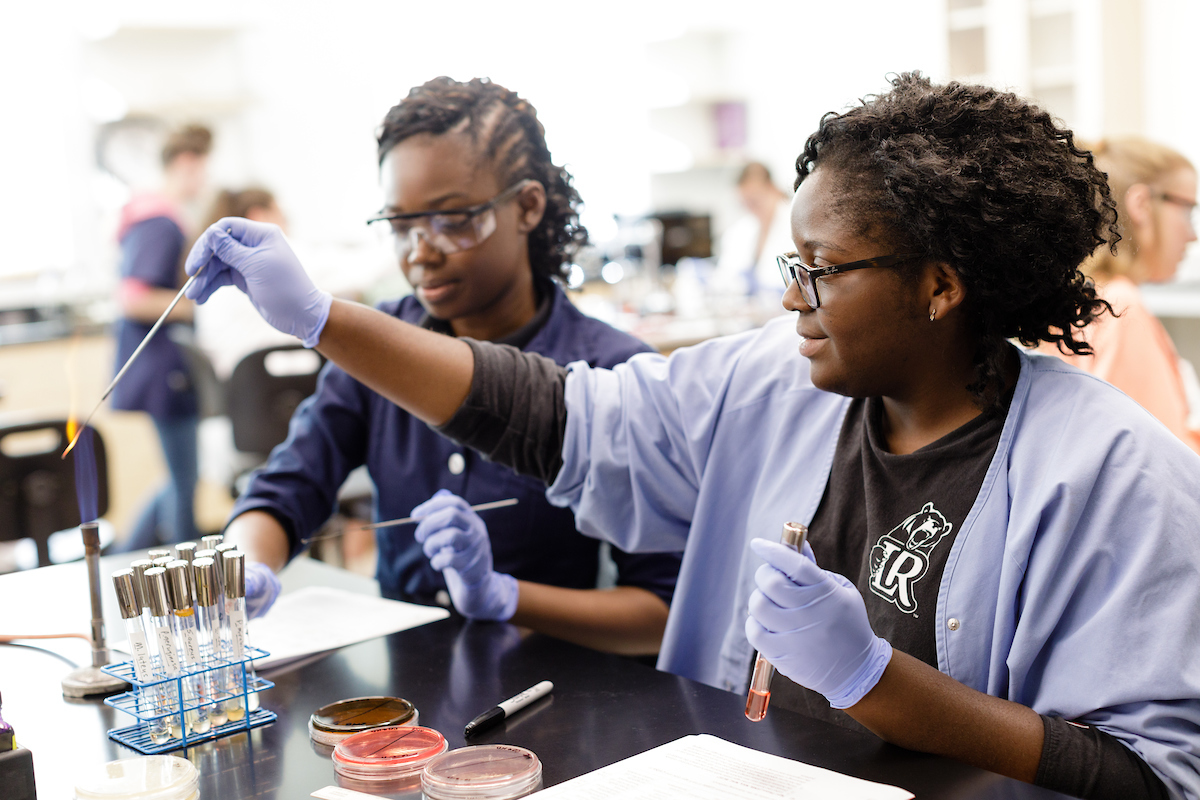 Two students work on chemistry lab assignment with burner and test tubes