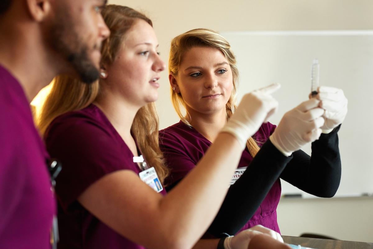 Nursing students in scrubs hold up and examine test tube during nursing lab