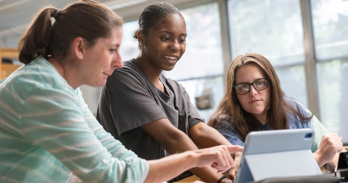 Professor works with two students in physics lab